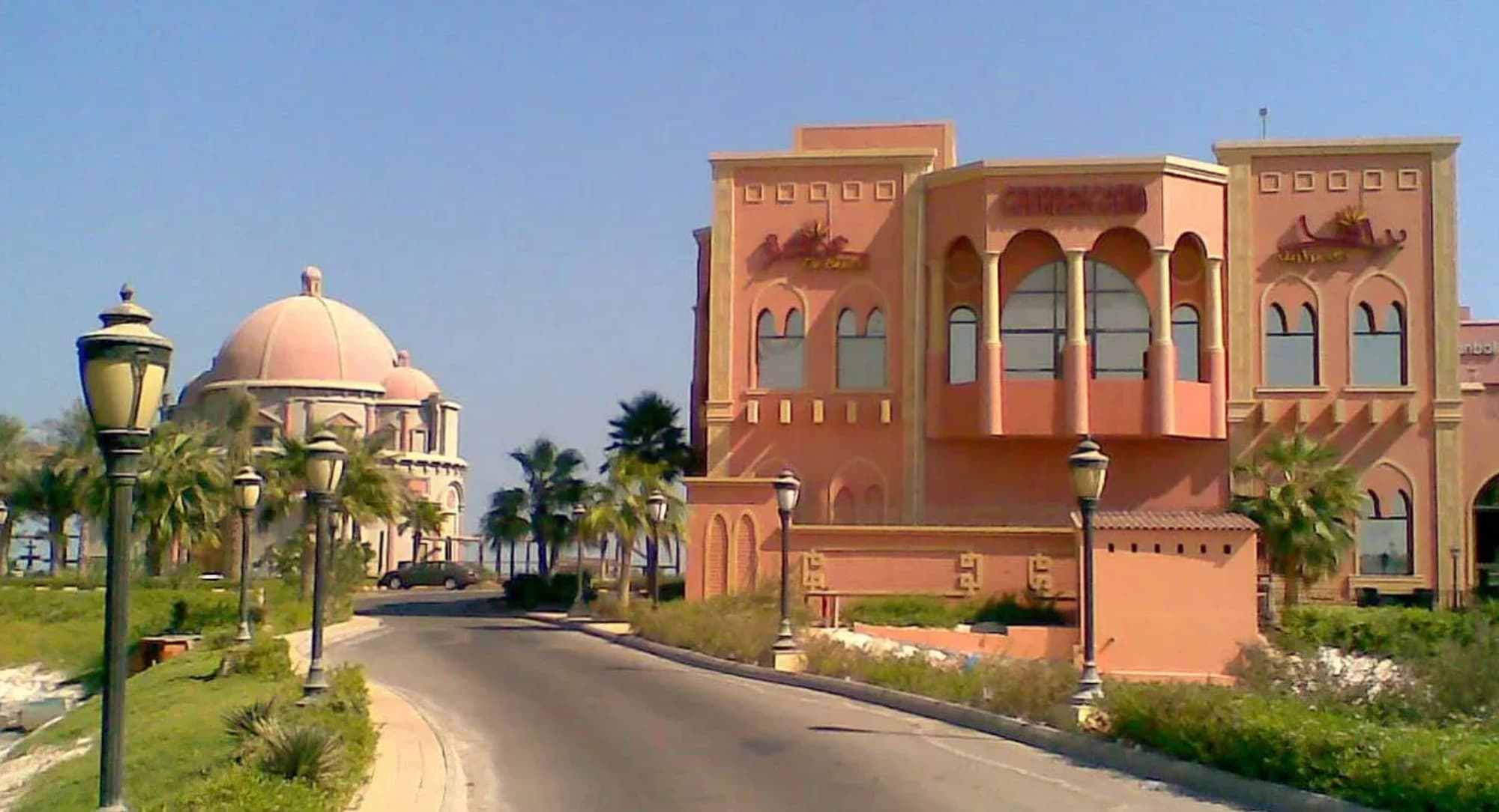 Domed and arched coral-pink buildings beside a palm-lined road in Saudi Arabia